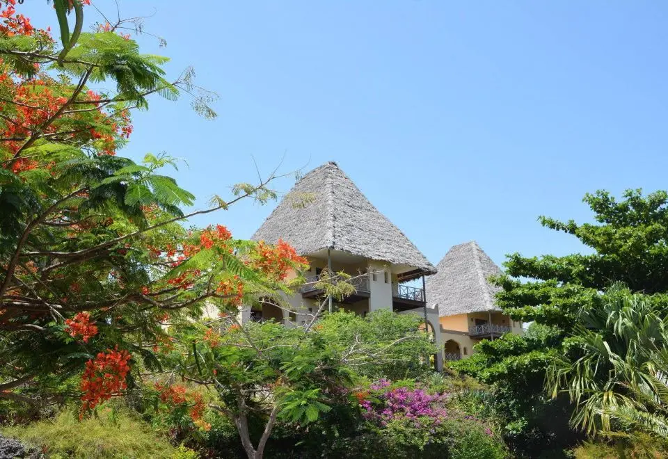 Bungalows de cobertura em colmo entre jardins floridos no Neptune Pwani Beach Resort & Spa