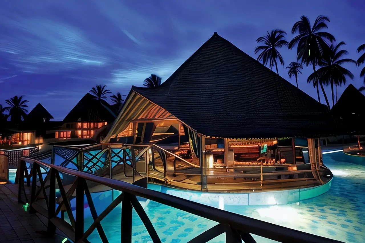 Ponte sobre a piscina junto ao bar de cobertura em colmo do Neptune Pwani Beach Resort & Spa à noite
