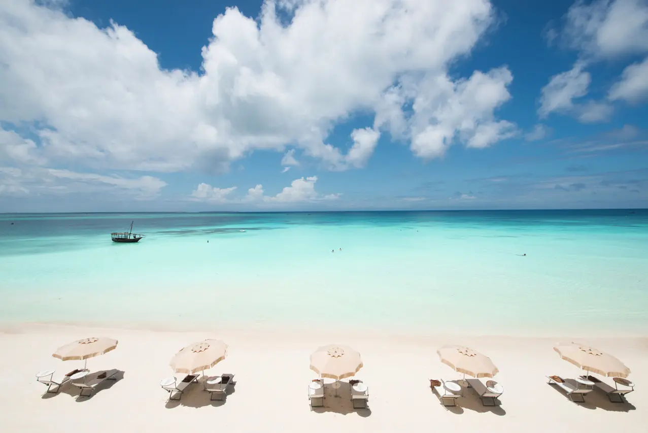 Espreguiçadeiras e guarda-sóis na praia do Hotel Riu Palace Zanzibar, com um dhow no mar