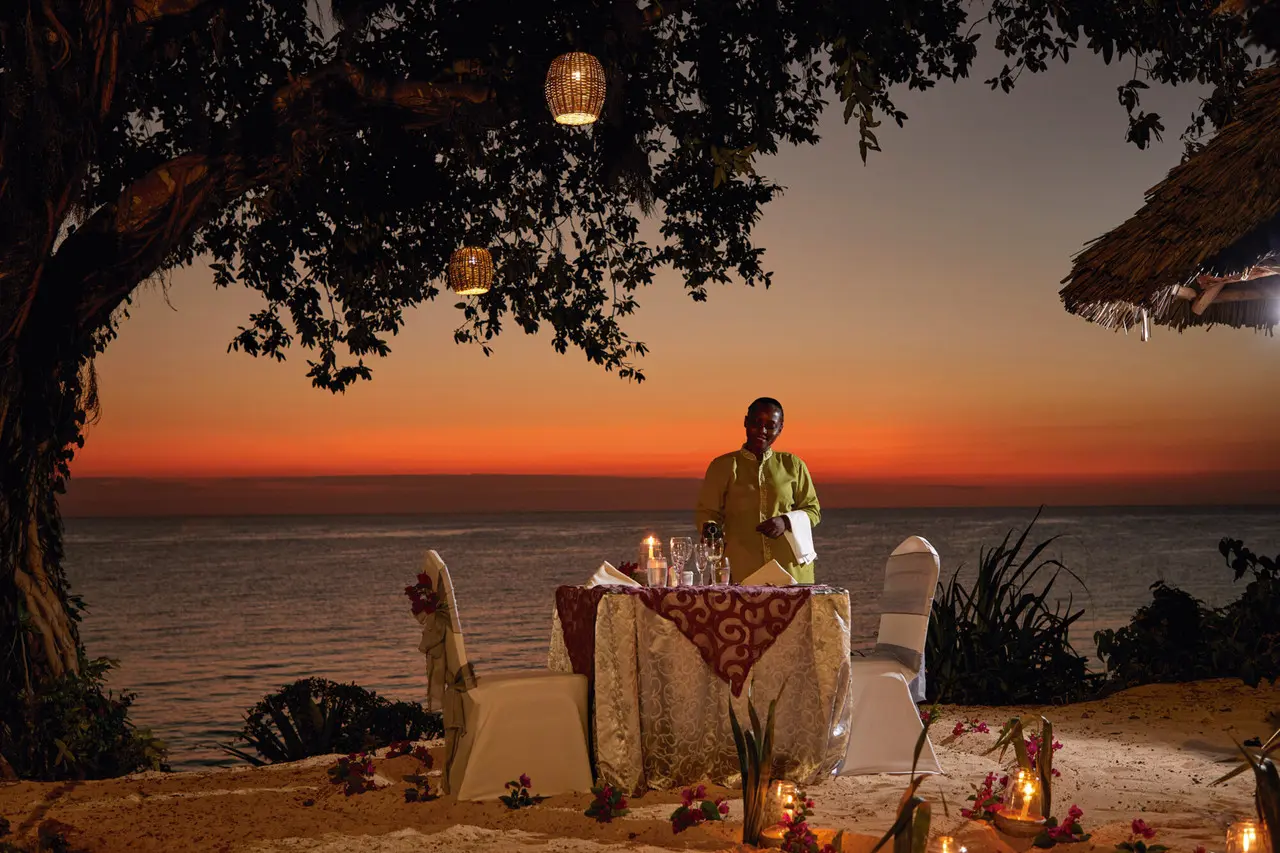 Mesa de jantar preparada junto ao mar no Hotel Riu Palace Zanzibar ao pôr do sol